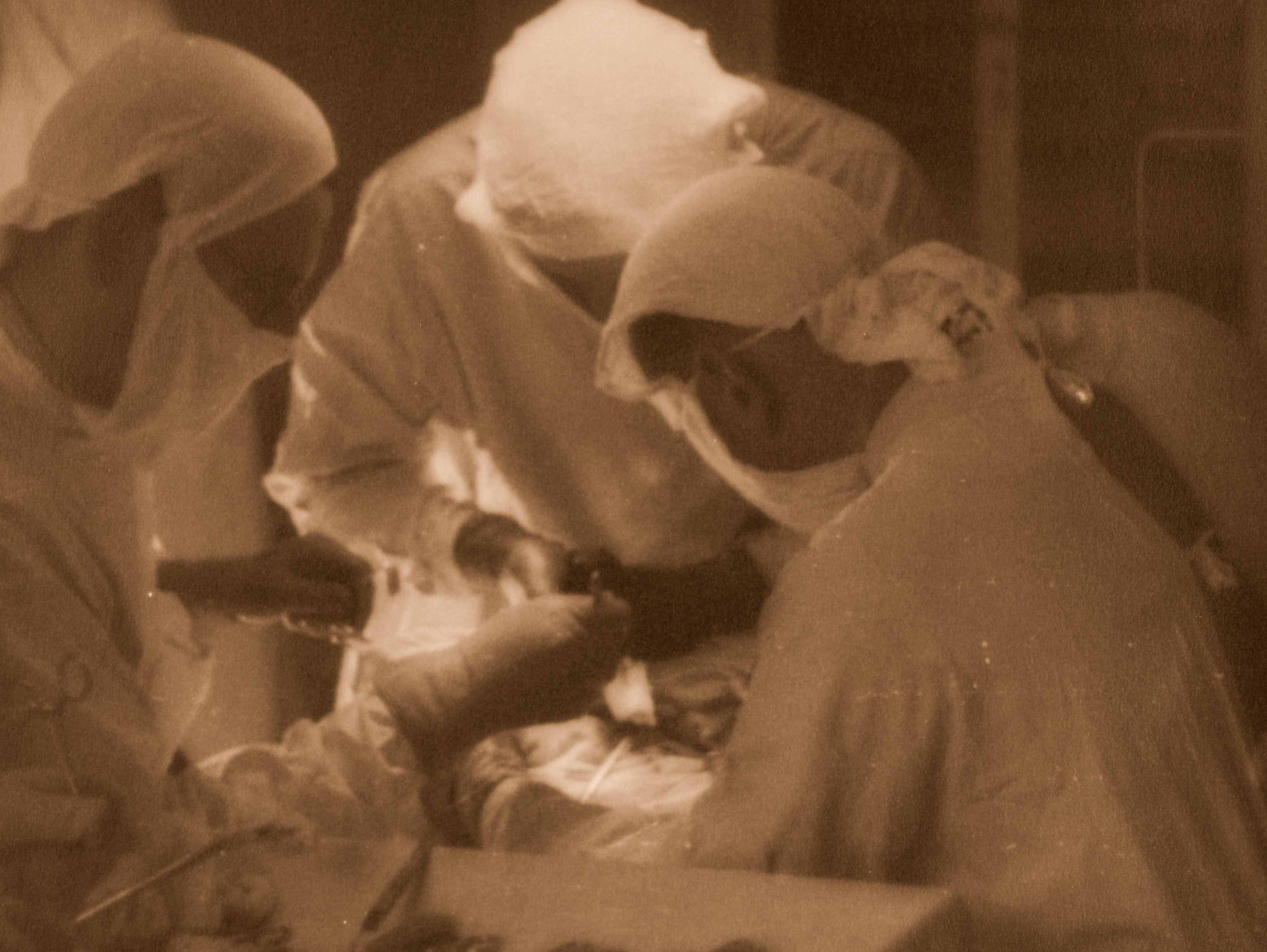 Kilka os&oacute;b w ubraniach medycznych pochylonych nad stołem operacyjnym. Zdjęcie archiwalne